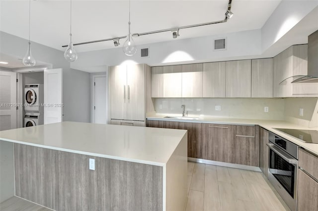 kitchen with stainless steel oven, a center island, tasteful backsplash, stacked washer / drying machine, and black electric stovetop