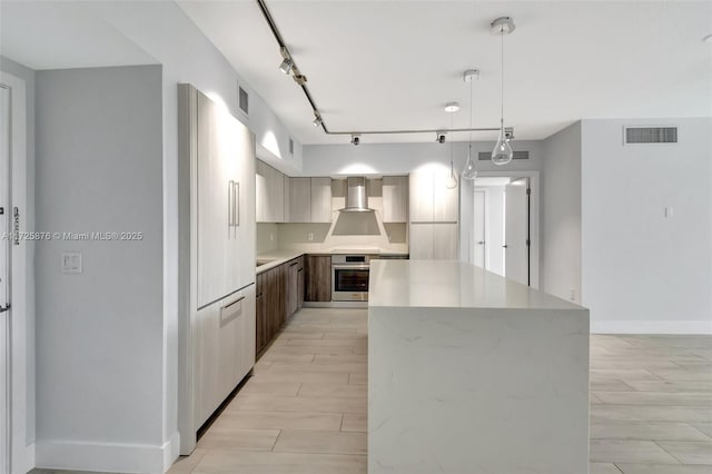 kitchen featuring oven, a center island, wall chimney exhaust hood, rail lighting, and pendant lighting