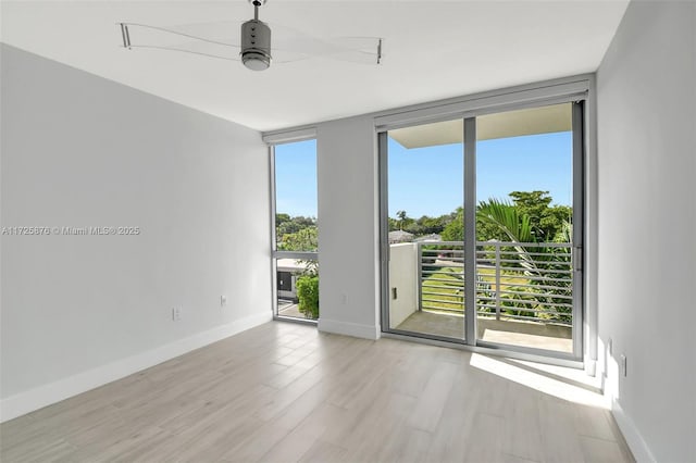 empty room with ceiling fan, a wall of windows, and light hardwood / wood-style flooring