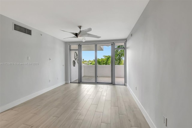 spare room featuring light wood-type flooring, ceiling fan, and expansive windows