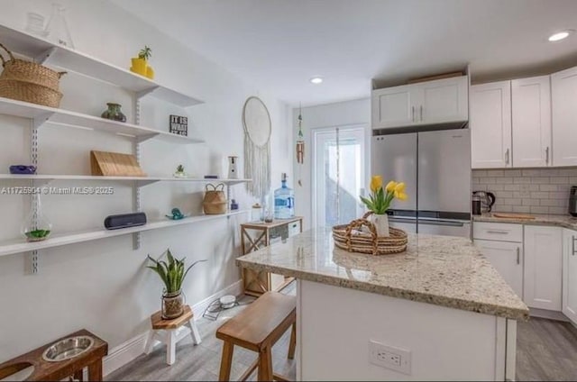 kitchen with light stone countertops, white cabinetry, light wood-type flooring, and stainless steel refrigerator