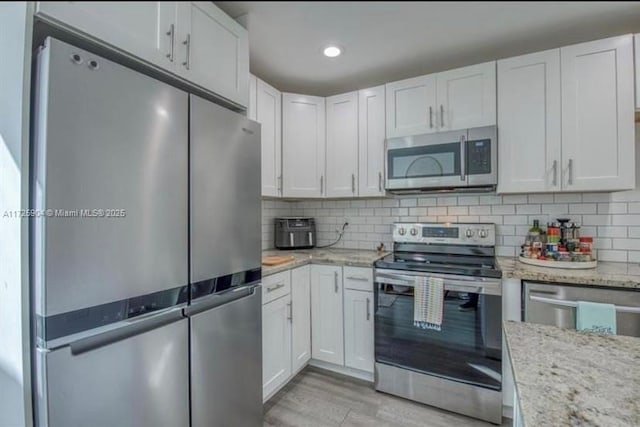 kitchen featuring backsplash, appliances with stainless steel finishes, light stone counters, and white cabinetry