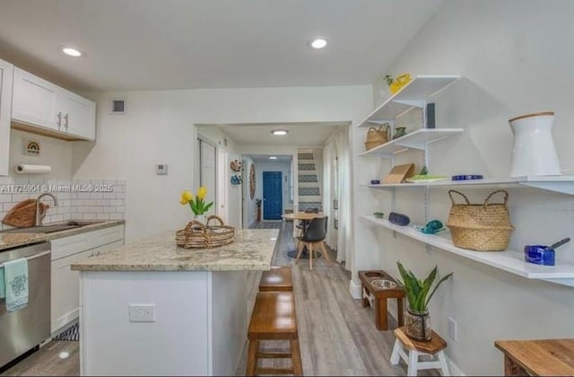 kitchen with light hardwood / wood-style floors, light stone countertops, stainless steel dishwasher, white cabinets, and sink