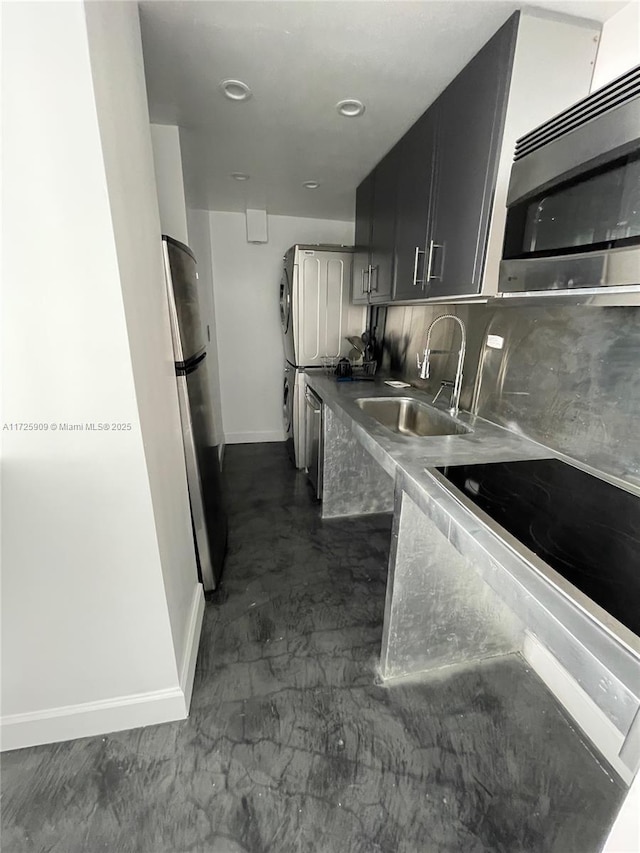 kitchen featuring tasteful backsplash, stacked washer and dryer, stainless steel appliances, and sink