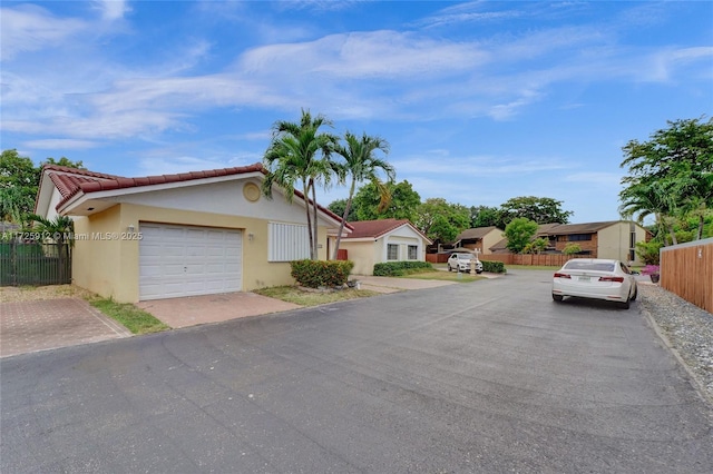 view of front of property featuring stucco siding, driveway, fence, a garage, and a tiled roof