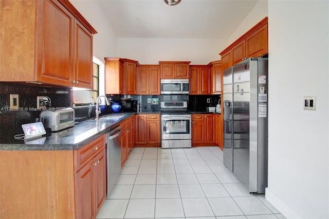 kitchen with light tile patterned floors, brown cabinetry, a sink, decorative backsplash, and stainless steel appliances