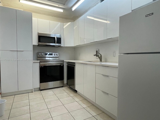 kitchen with sink, stainless steel appliances, light tile patterned flooring, and white cabinetry