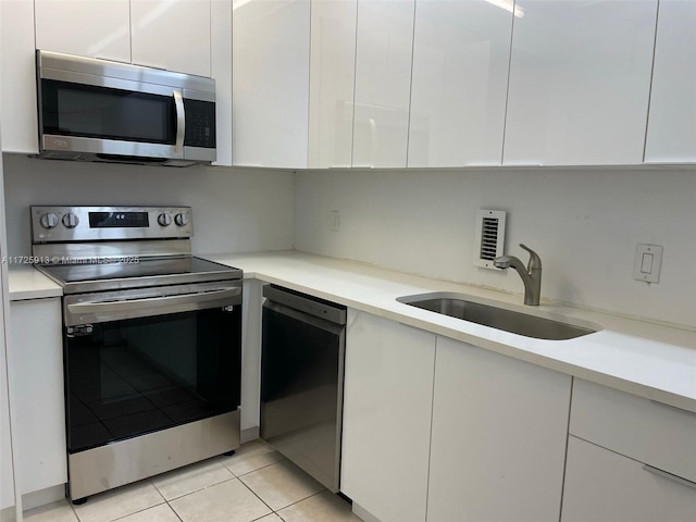 kitchen with appliances with stainless steel finishes, white cabinets, sink, and light tile patterned floors