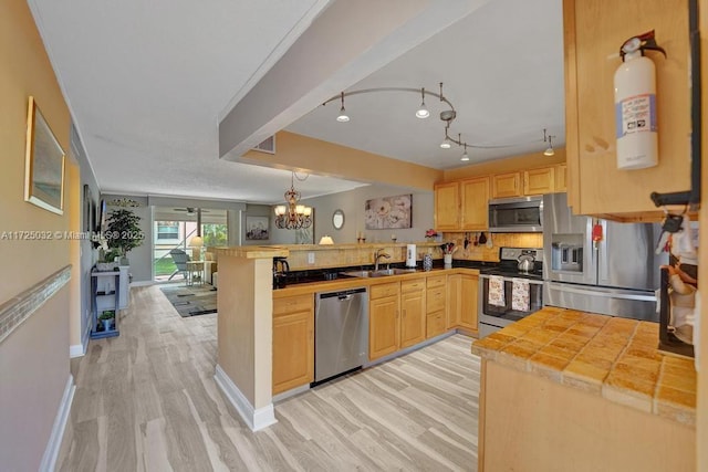 kitchen featuring kitchen peninsula, light brown cabinetry, light hardwood / wood-style floors, appliances with stainless steel finishes, and sink