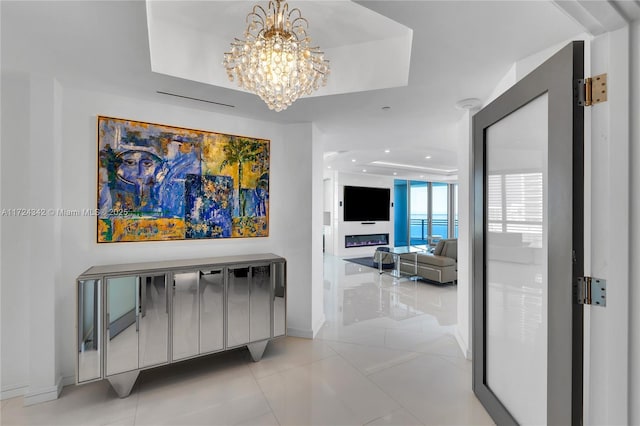 corridor featuring a tray ceiling, a chandelier, and light tile patterned floors