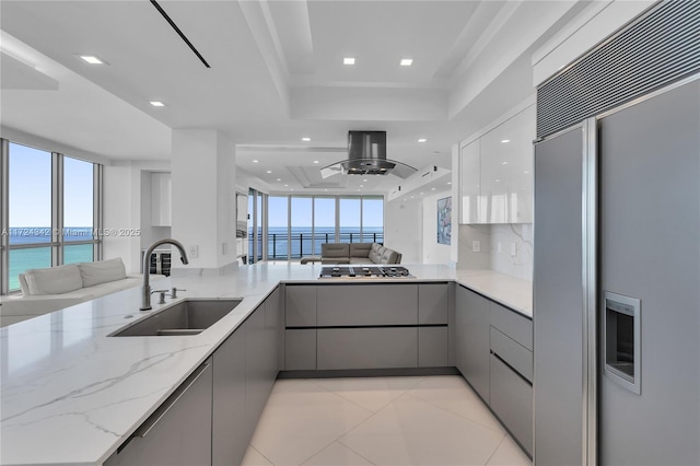 kitchen featuring sink, a water view, light stone counters, paneled refrigerator, and a tray ceiling