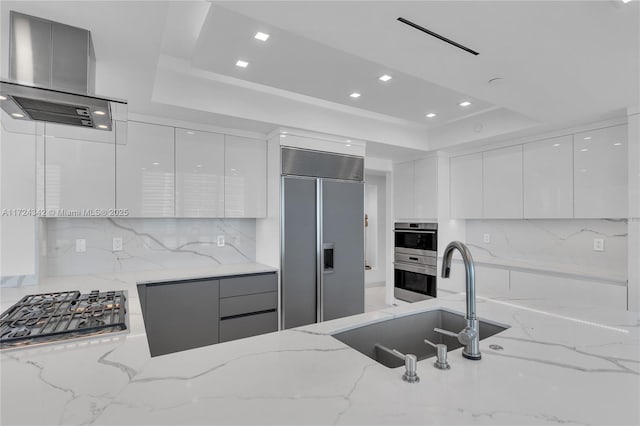 kitchen with sink, white cabinetry, stainless steel appliances, a tray ceiling, and light stone countertops