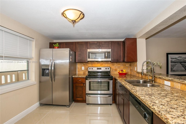 kitchen with light tile patterned floors, tasteful backsplash, light stone countertops, stainless steel appliances, and a sink