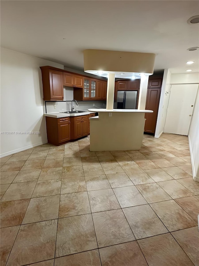 kitchen with a sink, light countertops, glass insert cabinets, stainless steel fridge, and a center island