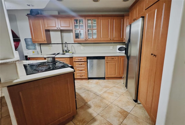 kitchen featuring light tile patterned flooring, a sink, light countertops, glass insert cabinets, and appliances with stainless steel finishes