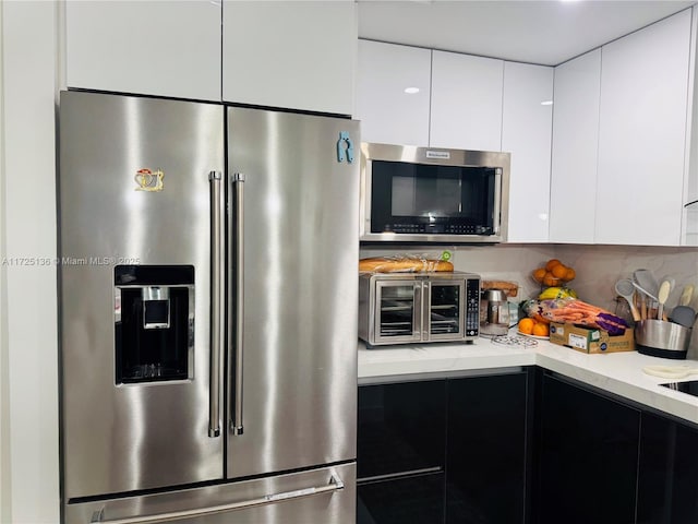 kitchen featuring light stone counters, stainless steel appliances, backsplash, and white cabinetry