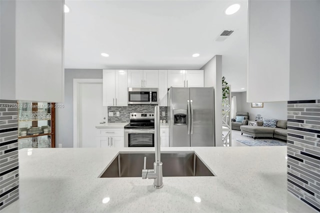 kitchen with stainless steel appliances, sink, white cabinets, backsplash, and light stone countertops