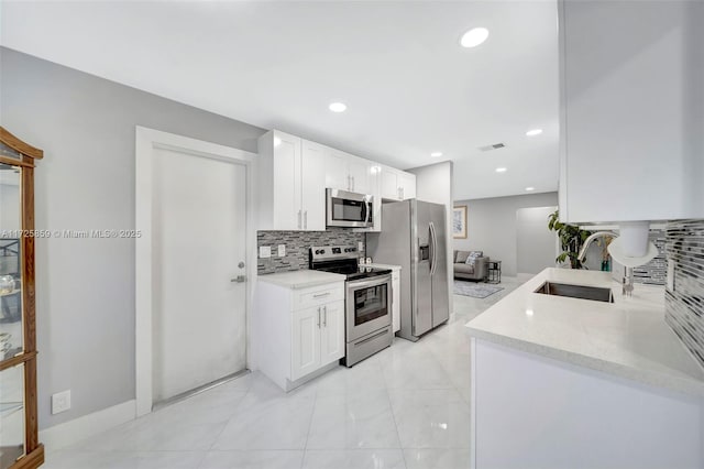 kitchen with stainless steel appliances, white cabinetry, sink, and light stone countertops