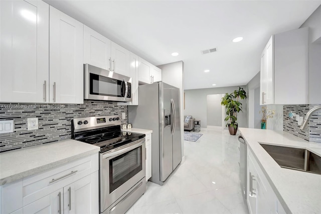 kitchen with appliances with stainless steel finishes, light stone counters, sink, white cabinetry, and backsplash