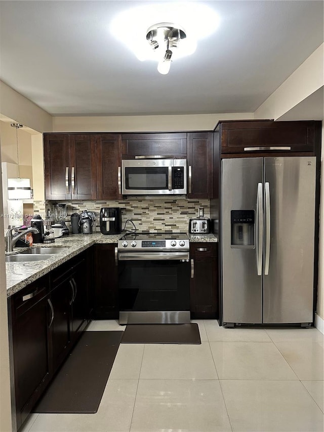 kitchen with light stone countertops, stainless steel appliances, decorative backsplash, light tile patterned flooring, and sink