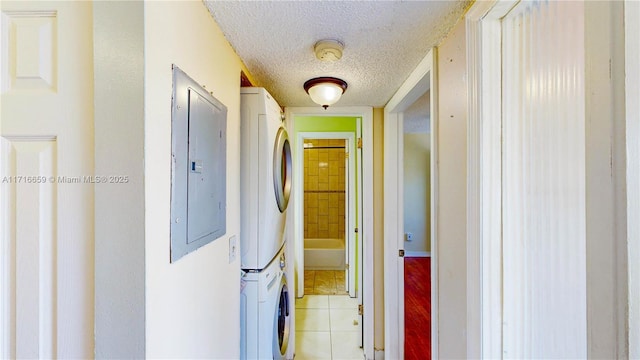 corridor featuring light tile patterned floors, electric panel, stacked washer and clothes dryer, and a textured ceiling