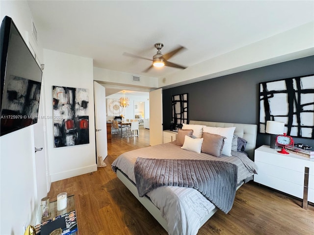 bedroom featuring ceiling fan with notable chandelier and hardwood / wood-style flooring