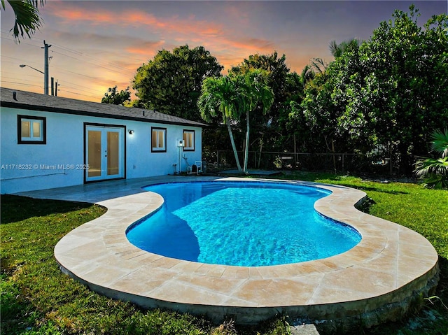 pool at dusk featuring french doors, a lawn, and a patio area