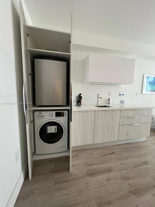 clothes washing area featuring stacked washing maching and dryer, sink, and light hardwood / wood-style floors