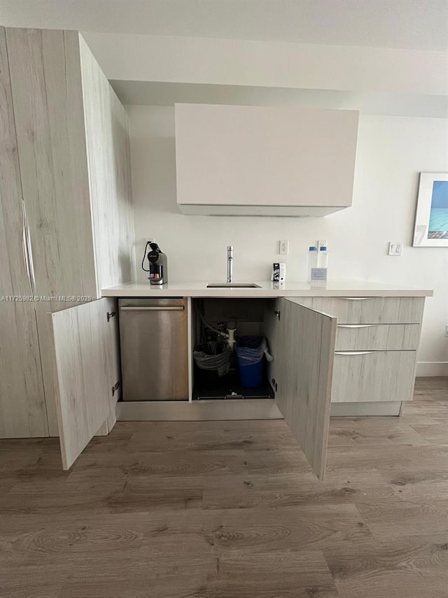 bar with stainless steel dishwasher, light brown cabinetry, sink, and light hardwood / wood-style flooring