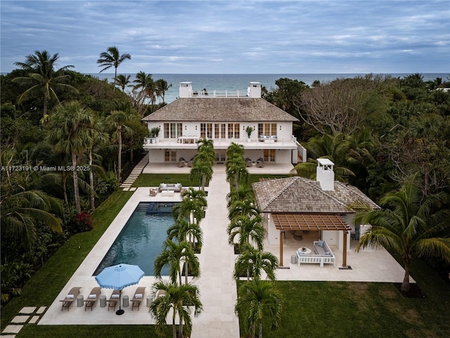 back of property with a balcony, exterior bar, a water view, a patio, and a yard