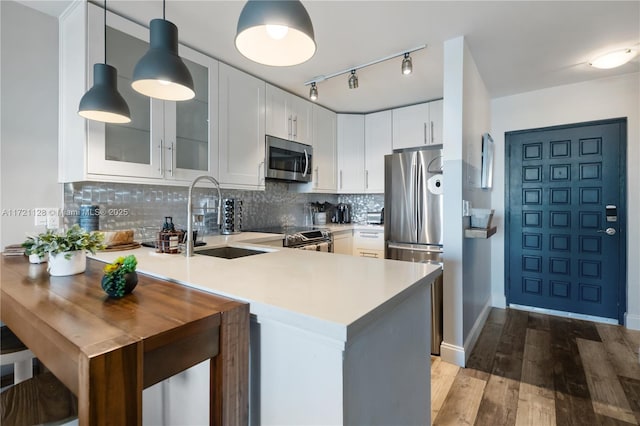 kitchen with kitchen peninsula, hanging light fixtures, stainless steel appliances, white cabinets, and sink