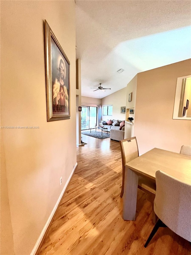 dining room with a textured ceiling, ceiling fan, vaulted ceiling, and light hardwood / wood-style flooring