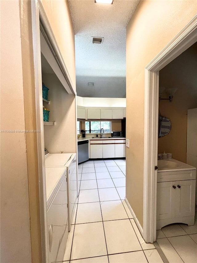 hall with a textured ceiling, separate washer and dryer, light tile patterned floors, and sink