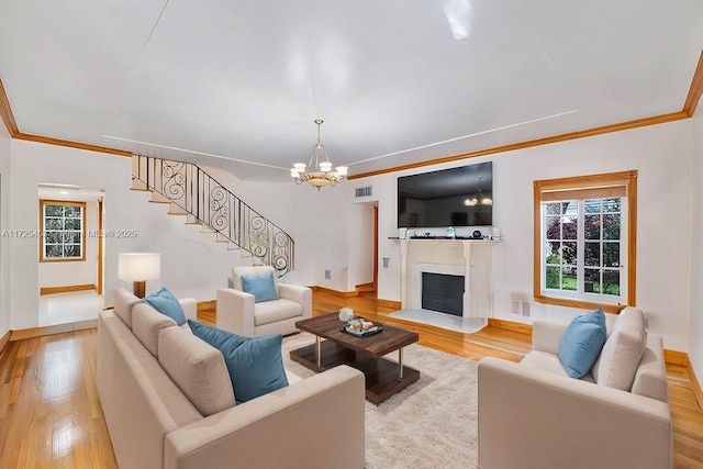 living room featuring a notable chandelier, crown molding, a fireplace, and light wood-type flooring