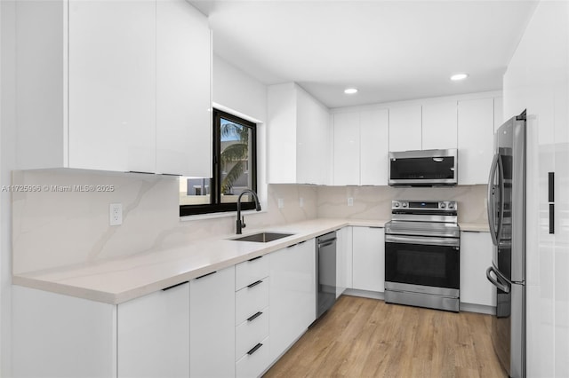 kitchen with decorative backsplash, sink, white cabinetry, light wood-type flooring, and appliances with stainless steel finishes