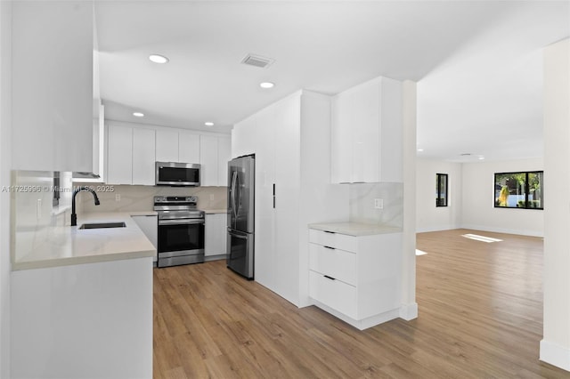 kitchen with decorative backsplash, sink, light wood-type flooring, stainless steel appliances, and white cabinets