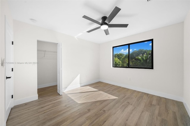 unfurnished bedroom with a spacious closet, ceiling fan, a closet, and light wood-type flooring