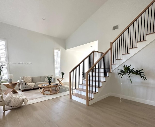 stairs with high vaulted ceiling, a healthy amount of sunlight, and hardwood / wood-style floors