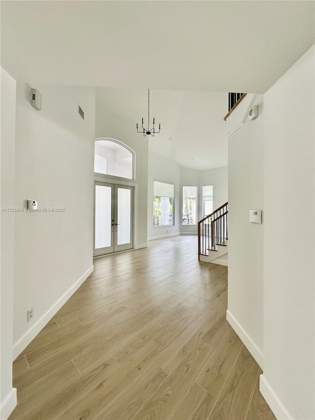 unfurnished living room with french doors, a high ceiling, a chandelier, and light hardwood / wood-style flooring