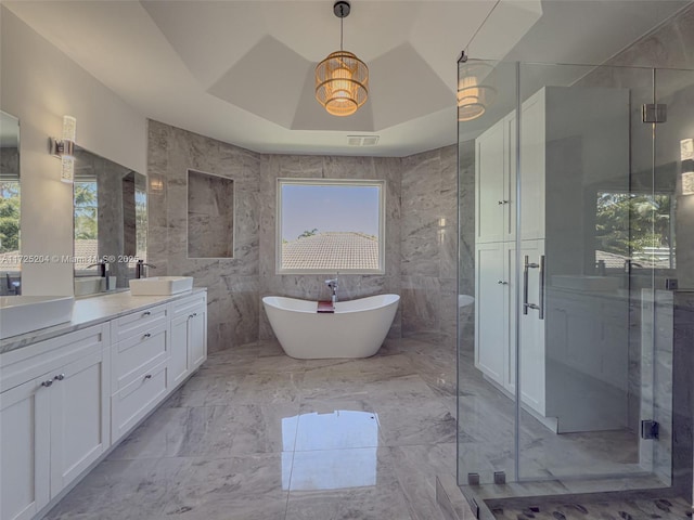 full bath featuring tile walls, a raised ceiling, vanity, a shower stall, and a freestanding tub