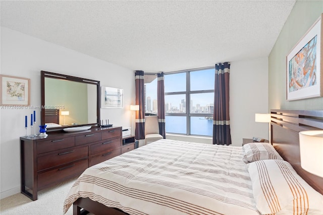 bedroom featuring a textured ceiling, a water view, and light carpet