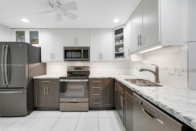 kitchen with stainless steel appliances, sink, white cabinets, dark brown cabinets, and light stone countertops