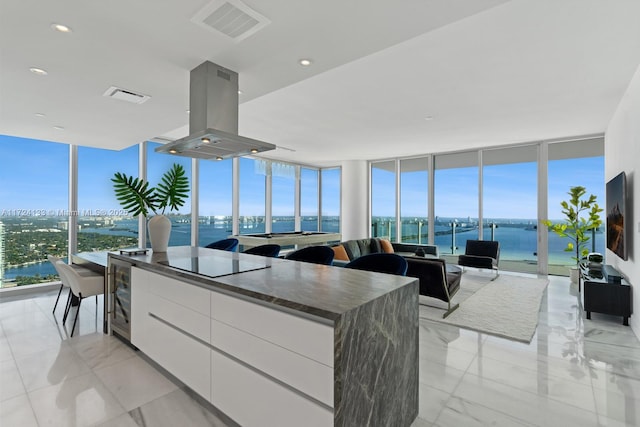 kitchen with island exhaust hood, beverage cooler, a wall of windows, black electric stovetop, and white cabinetry