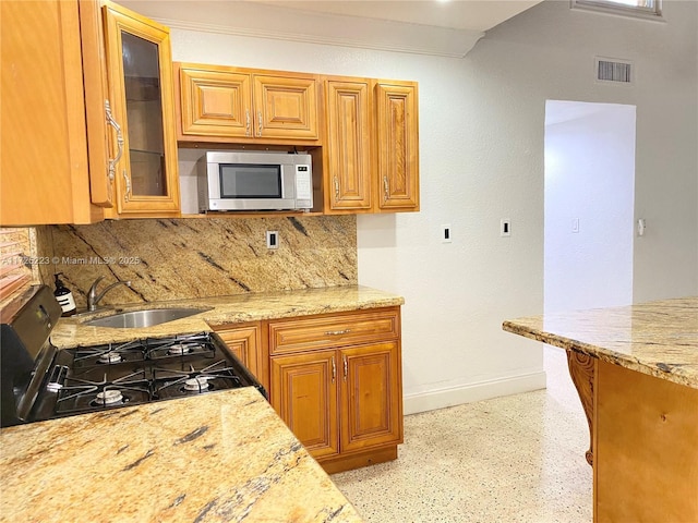 kitchen with sink, backsplash, light stone counters, crown molding, and gas range oven