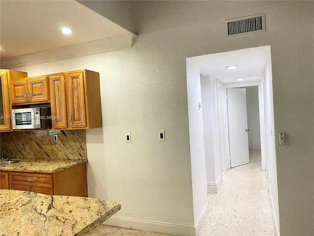 6181 SW 20th St, West Miami, FL 33155 - kitchen with stainless steel microwave, baseboards, brown cabinetry, light stone counters, and backsplash