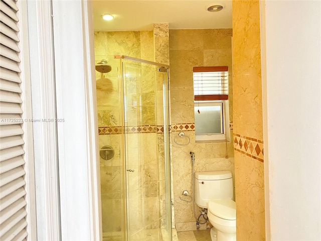 bathroom featuring a shower with door, tile walls, and toilet