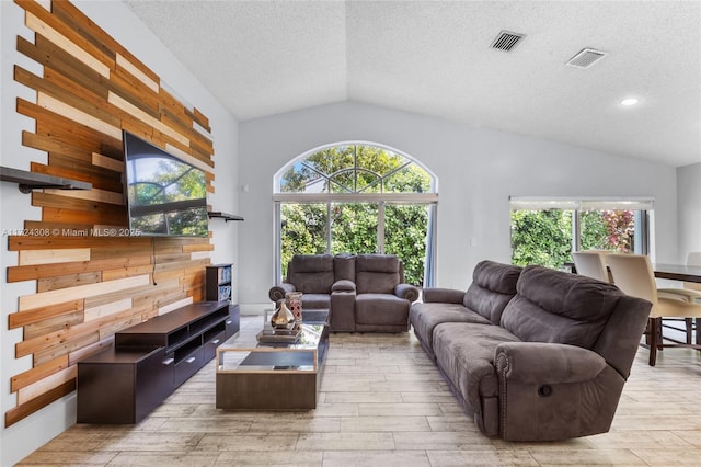 living room with a textured ceiling, wooden walls, a wealth of natural light, and vaulted ceiling