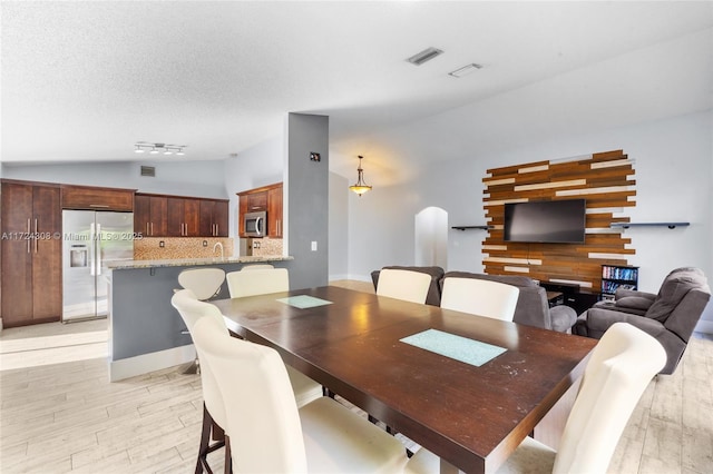 dining room featuring a textured ceiling, light hardwood / wood-style flooring, and vaulted ceiling