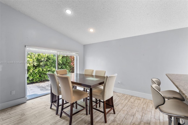 dining room featuring lofted ceiling, a textured ceiling, and light hardwood / wood-style floors