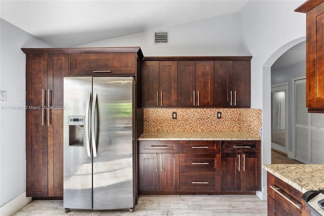 kitchen featuring light stone countertops, vaulted ceiling, backsplash, and stainless steel refrigerator with ice dispenser